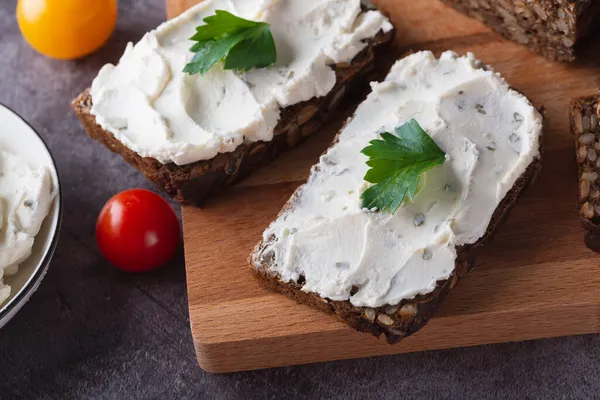 Rågbröd på en skärbräda av trä med ostmassa och ricotta och örter. — Stockfoto