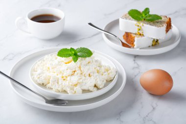 Bir kase taze süzme peynir, kek, yumurta ve kahve.