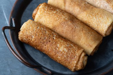 Gri arka planda süzme peynirle doldurulmuş ince krepler ya da krepler