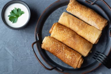 Gri arka planda süzme peynirle doldurulmuş ince krepler ya da krepler