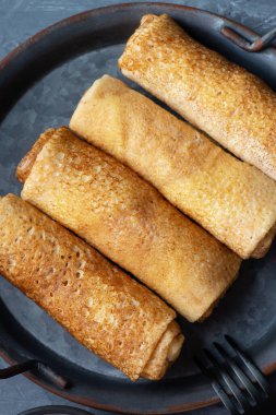 Gri arka planda süzme peynirle doldurulmuş ince krepler ya da krepler