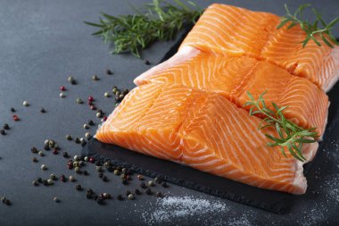 Çiğ somon fileto ve yemek pişirmek için malzemeler, baharatlar ve gri arka planda bitkiler..