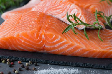 Çiğ somon fileto ve yemek pişirmek için malzemeler, baharatlar ve karanlık bir arka planda otlar..