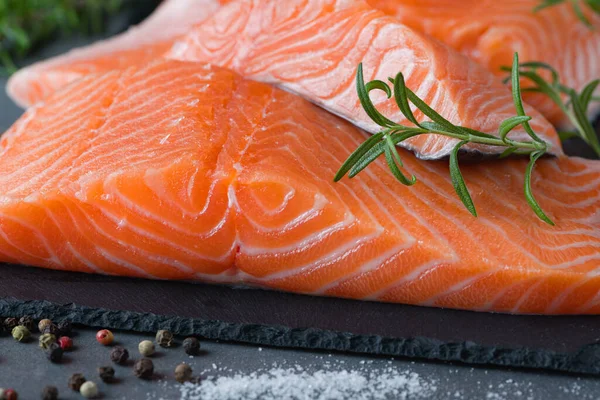 Çiğ somon fileto ve yemek pişirmek için malzemeler, baharatlar ve karanlık bir arka planda otlar..