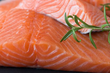 Çiğ somon fileto ve yemek pişirmek için malzemeler, baharatlar ve karanlık bir arka planda otlar.