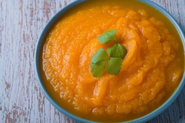 Mavi ahşap bir masada bir kase balkabağı çorbası