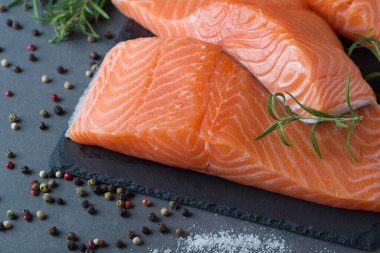 Çiğ somon fileto ve yemek pişirmek için malzemeler, baharatlar ve karanlık bir arka planda otlar..