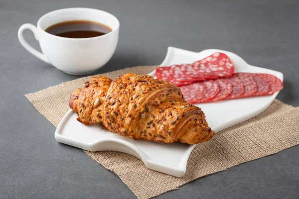 Frisches Croissant-Sandwich mit Wurst und Kaffee auf grauem Tisch — Stockfoto