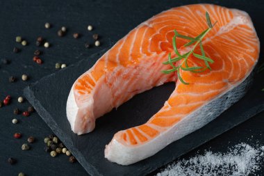 Çiğ somon fileto ve yemek pişirmek için malzemeler, baharatlar ve karanlık bir arka planda otlar.