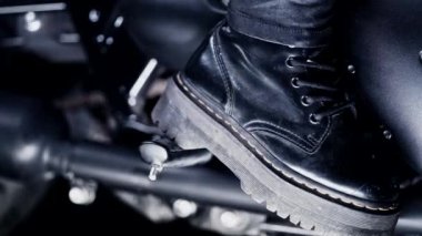 Klasik bisikletin üzerinde oturan şık motosikletli kadının bacakları. Siyah eski model motosiklet. Gaddar, deri asker botları giymiş bir kadın. Yepyeni bir motosikletin klasik tasarımının ayrıntıları.