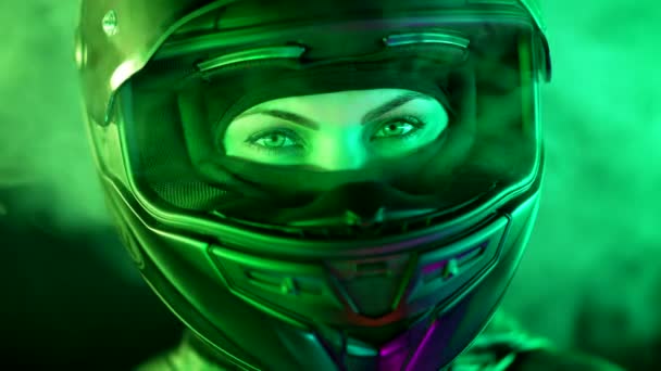 오토바이를 타는 젊은 여성 이 폐색 오토바이 헬멧을 쓰고 있습니다. 운전기사는 밤에 연기나 수증기를 머금은 다채 로운 네온 조명 아래 카메라를 찾는다. 놀라운 미적 인물 사진. — 비디오