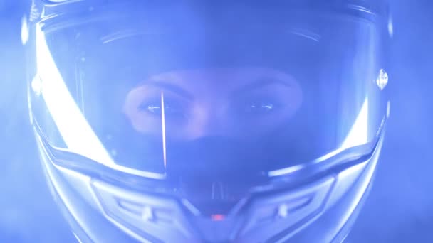 Mulher motociclista em capacete de motocicleta fechado em fumaça ou neblina. Motorista motociclista olhando para câmera sob luz de cor azul à noite. Retrato estético épico. — Vídeo de Stock