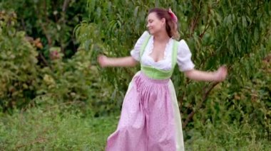 Dirndl 'deki komik kadın. Geleneksel festival elbisesi, elma bahçesi arka planında dans ediyor. Dans, maskaralık, pozitif ve eski moda konsept.