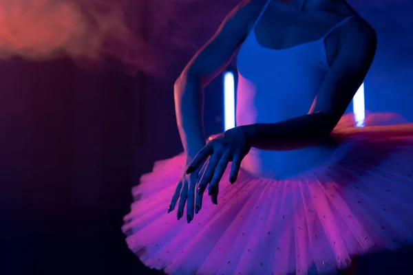Kecses felismerhetetlen balerina tütü ruhában, kézzel táncol, füsttel színezi a neon fényt. Nő hosszú, sötét körmökkel és szellős szoknyával. Stúdió felvétel. Művészeti koncepció. — Stock Fotó
