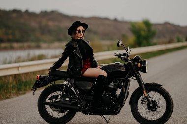 Motosikletli kadın mini etekli retro-stil motosikletin üzerinde oturuyor. Yoldaki çizmeli seksi kadın şoför. Trip, hız, özgürlük kavramı.