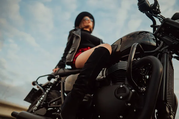 Mujer motociclista irreconocible en mini falda sentada en una motocicleta de estilo retro. Conductora sexy con botas de chaqueta en la carretera. Viaje, velocidad, concepto de libertad. —  Fotos de Stock
