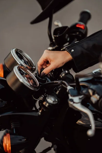 Female motorcyclist turns on ignition of modern classic motorcycle. Arrows and indicators on speedometer dashboard. Close-up side view. — Stock Photo, Image