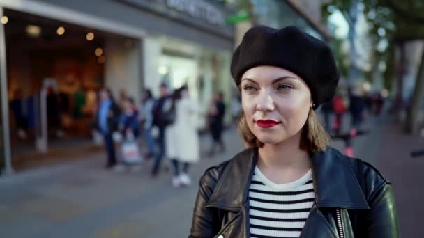 Muotokuva trendikäs eurooppalainen nainen hattu seisoo kiireinen kaupungin kadulla. Lady hymyilevä, moderni kaupunkiasu, nahkatakki ja punaiset huulet. — kuvapankkivideo