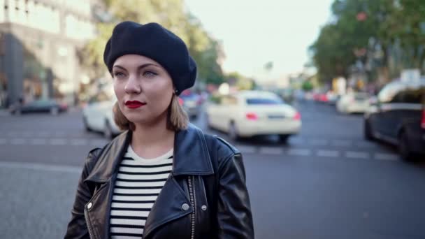 Retrato de jovem elegante na boina em pé na movimentada rua da cidade. Senhora sorrindo, roupa urbana moderna, jaqueta de couro e lábios vermelhos. — Vídeo de Stock