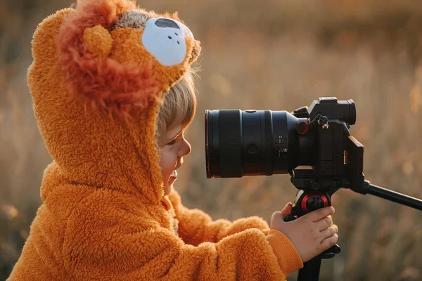 Roztomilý batole v kostýmu oranžového lva, usmívá se na objektivy zblízka. Dítě se podívá na profesionální digitální fotoaparát fotografa v přírodě. — Stock fotografie