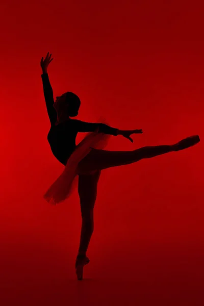 Schöne Ballerina auf rotem Hintergrund tanzt Ballett. Die Frau führt sanfte Bewegungen aus. Sinnliche Tänzerin im Tutu-Kleid auf der Bühne unter Neonlicht.. — Stockfoto