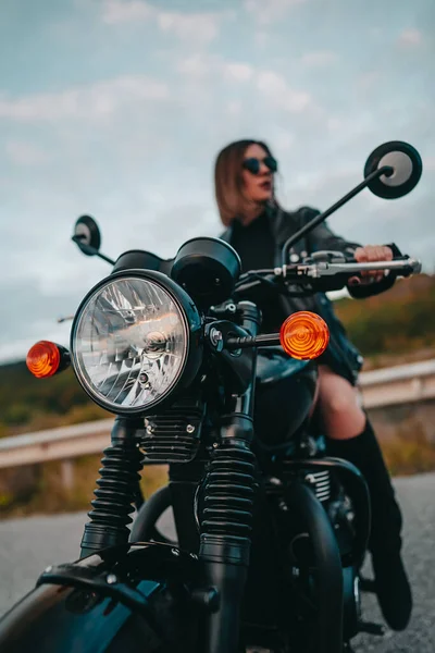 Mujer motociclista sentada en motocicleta de estilo retro. Conductora sexy con botas de chaqueta en la carretera. Viaje, velocidad, concepto de libertad. —  Fotos de Stock