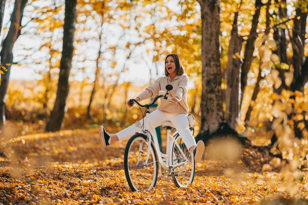 年轻漂亮的女人骑着老式的白色自行车在秋天的公园里。女士享受橙色自然秋天的背景. — 图库照片