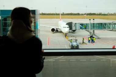 Havaalanında panoramik büyük pencerenin yanında duran kadın gezgin. Bayan uçuşu bekliyor. Seyahat, yolculuk, uçak konsepti.