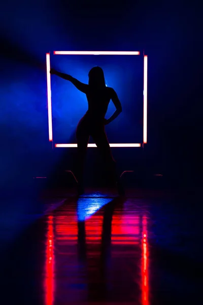 Silhouette of sexy woman dancing on glowing square of led red lamps background. She looks seductively. Sexy outfit . Blue smoky studio. — Stock Photo, Image