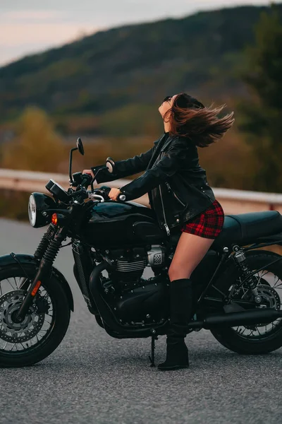 Kendine güvenen motosikletli kadın portresi mini etekli, deri ceketli retro-stil motosikletli. Otobanda çizmeli çekici bir sürücü. Trip, hız, tarz, feminizm kavramı.