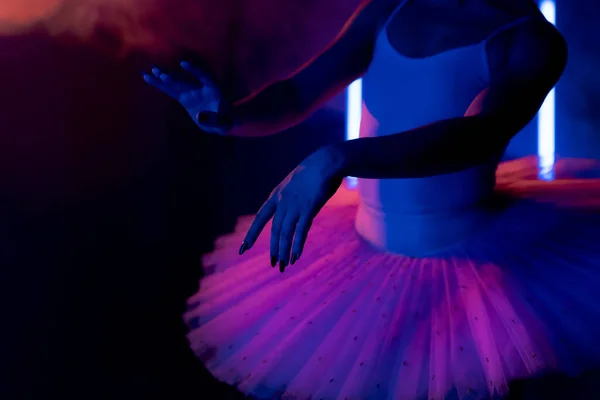 Kecses felismerhetetlen balerina tütü ruhában, kézzel táncol, füsttel színezi a neon fényt. Nő hosszú, sötét körmökkel és szellős szoknyával. Stúdió felvétel. Művészeti koncepció. — Stock Fotó