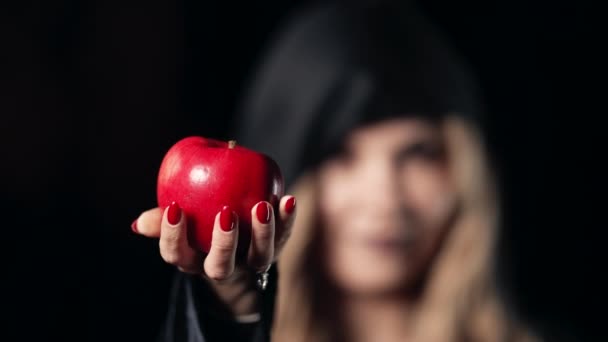 Woman as witch with an evil grin laugh in black offers red apple as symbol of temptation, poison. Fairy tale white snow concept, halloween, cosplay. — Stock Video