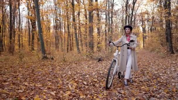 Wanita muda berjas hujan klasik dengan sepeda retro di taman musim gugur kuning. Adegan menakjubkan gadis trendi di latar belakang alam. Moda transportasi yang ramah lingkungan — Stok Video