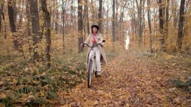 Güz parkında tek başına bisiklet süren genç bir kadının güzel portresi. Güneşli bir gün, ormanda altın yapraklar. Klasik beyaz bisikletteki moda kadın, sağlıklı yaşam tarzı, estetik görüntüler..