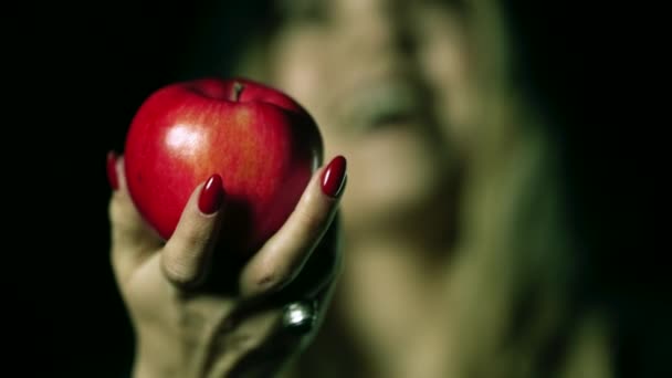 Mujer como bruja con una sonrisa malvada, risa en negro ofrece manzana roja como símbolo de tentación, veneno. cuento de hadas concepto de nieve blanca, halloween, cosplay. — Vídeos de Stock