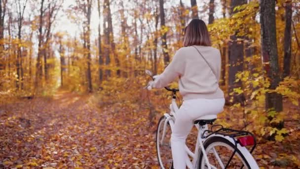 Młoda ładna kobieta jeżdżąca na retro-stylowym białym rowerze w złotym jesiennym parku. Niesamowita scena pani na tle natury. Zdrowy styl życia, jazda na rowerze, szczęście i beztroska koncepcja. — Wideo stockowe