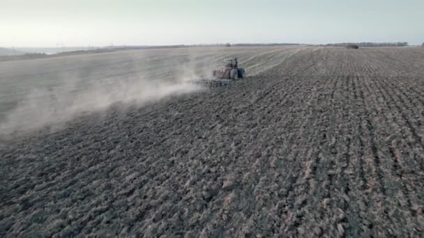 Drone tracking shot van landbouw trekker ploegen droge grond na het verzamelen van de oogst, pijler van stofpaden achter. Luchtfoto van agrarische natuurlijke seizoensgebonden werken. Schokkend concept. — Stockvideo