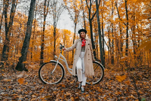 Jovem mulher em casaco de trincheira clássico com bicicleta retro no parque de outono amarelo. Cena incrível de menina na moda no fundo da natureza. Modo de transporte ecológico — Fotografia de Stock