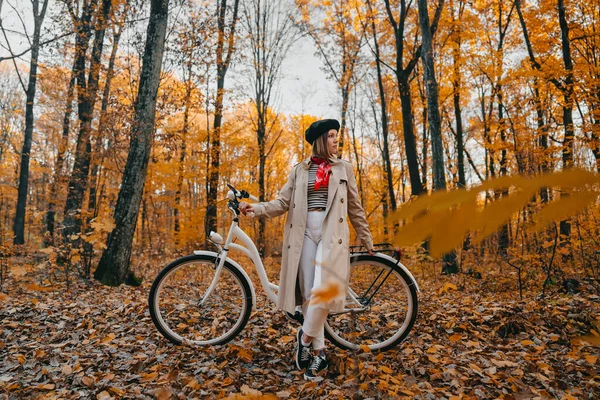 Młoda kobieta w klasycznym płaszczu z rowerem retro w żółtym jesiennym parku. Niesamowita scena modnej dziewczyny na tle natury. Przyjazny dla środowiska środek transportu — Zdjęcie stockowe