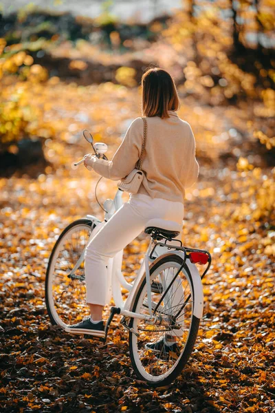 秋天公园里骑自行车的女人的美丽画像.阳光灿烂的日子,金黄的树叶在森林里.穿着老式白色自行车的时髦女士，健康的生活方式，美观的场面 — 图库照片