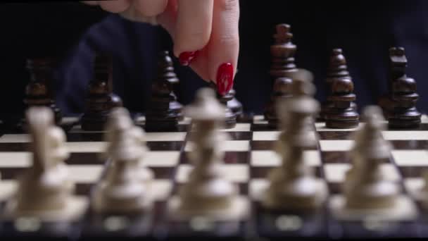 Kobieta gracz gra w gry planszowe inteligencji - drewniane szachy. Z bliska widok kobiecego ramienia z czerwonymi paznokciami porusza pionkiem pionka szachowego, pierwszy ruch. Sport, koncepcja strategii sukcesu. — Wideo stockowe