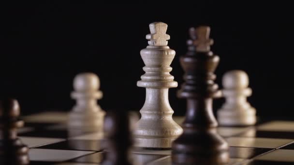 Svartvita schackkungar roterar på träskiva. Närbild av bitar på schackbrädet på mörk bakgrund. Sport, kamp, duell, rivaler koncept. — Stockvideo