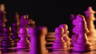 Tahta zeka oyunu - neon renkli ışık altında saat yönünde dönen tahta satranç - pembe ve sarı. Koyu arkaplanda satranç tahtasındaki taşların yakın görüntüsü. Spor, başarı stratejisi kavramı.