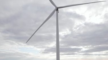 Bulutlu gökyüzünde dönen yel değirmeni arka planda. İHA görüntüsü, rüzgar türbinleriyle üretilen temiz yenilenebilir enerji. Açık ya da açık denizlerdeki büyük çiftlikte son sürat dönen bıçaklar. Alternatif yaşam tarzı.
