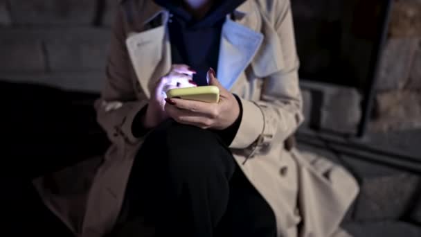 夜道でスマホを使う若い女性。石段の上に一人で座っている女性、彼女はモバイルデバイスでインターネットサーフィン。秋のシーズン。テクノロジー、ソーシャルアプリ、接続コンセプト — ストック動画