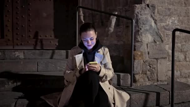 Junge Frau mit Smartphone auf nächtlicher Stadtstraße. Lady sitzt allein auf Steintreppen und surft mit ihrem Mobilgerät im Internet. Herbstzeit. Technologie, Social Apps, Verbindungskonzept — Stockvideo