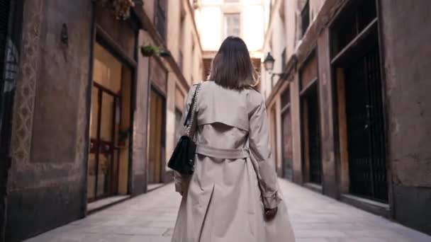 Vue arrière de la femme marchant seule dans le quartier gothique de Barcelone. Bâtiments anciens, rues étroites d'Europe. Voyager en automne, dame en trench coat. — Video