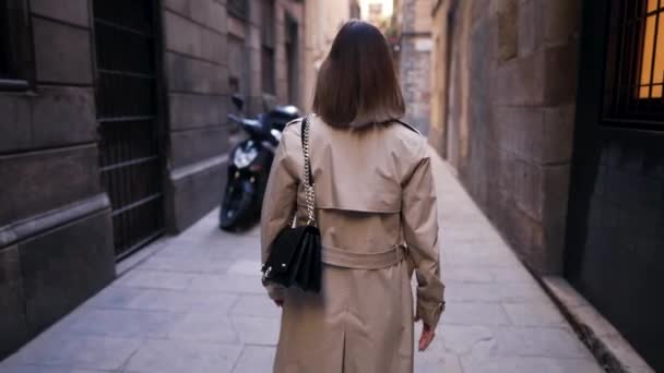 Unrecognizable stranger woman walking alone in empty narrow street. Autumn season.Busy lady in coat walking to office. Medieval european architecture, old buildings. Exploring Barcelona. — Stock Video