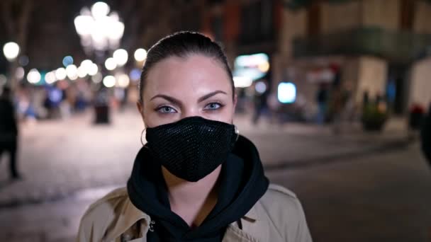 Retrato de mujer en máscara de protección facial en la calle de la ciudad de noche con iluminación. Estudiante o turista durante la cuarentena de covid-19 en la ajetreada ciudad.. — Vídeo de stock