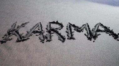 Karma kelimesi siyah kumsalda yazılmış, deniz veya okyanus dalgalarıyla sürüklenmiş. Sebep ve sonuç. Din kavramı, ezoterizm, Budizm, dünya uyumu ve evren dengesi.